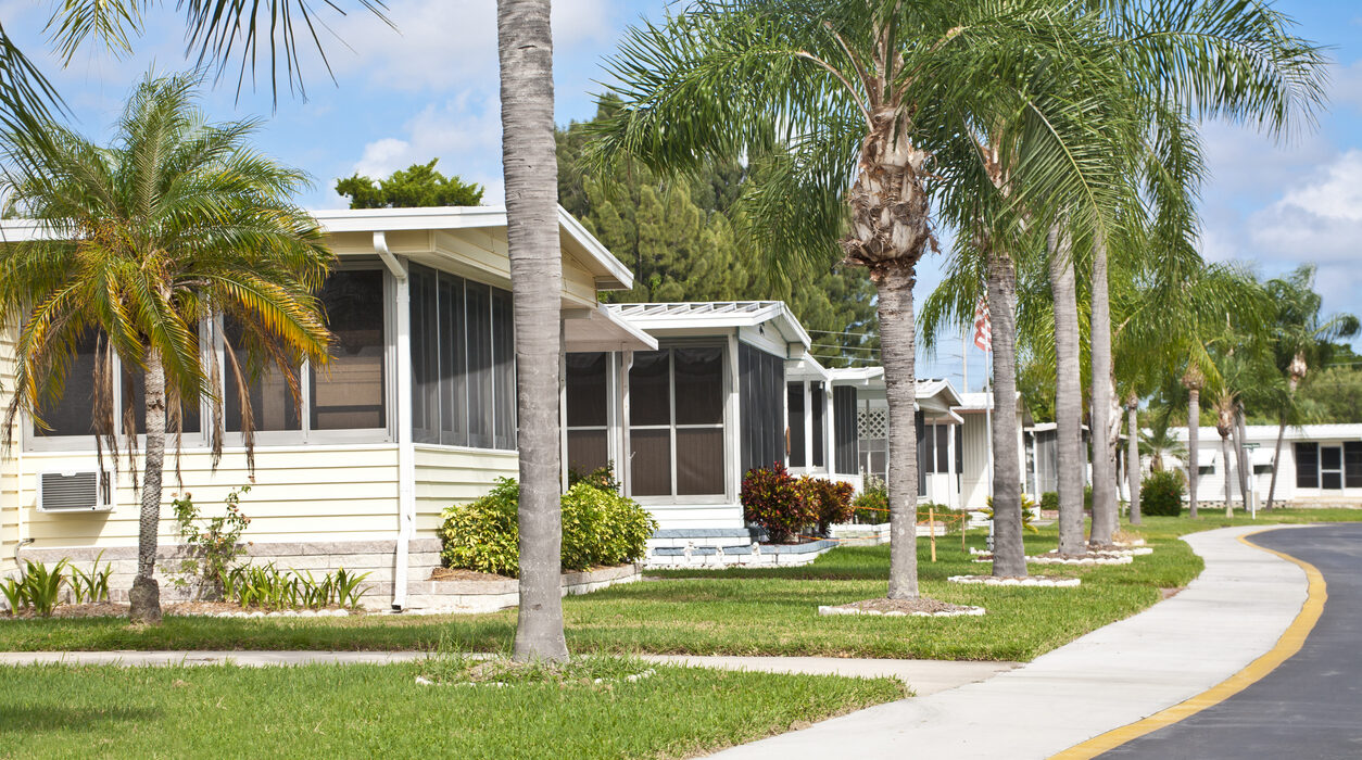 Mobile homes in a row located in a mobile home park in the tropics. Street view with palm trees and sidewalk. Caravan park.